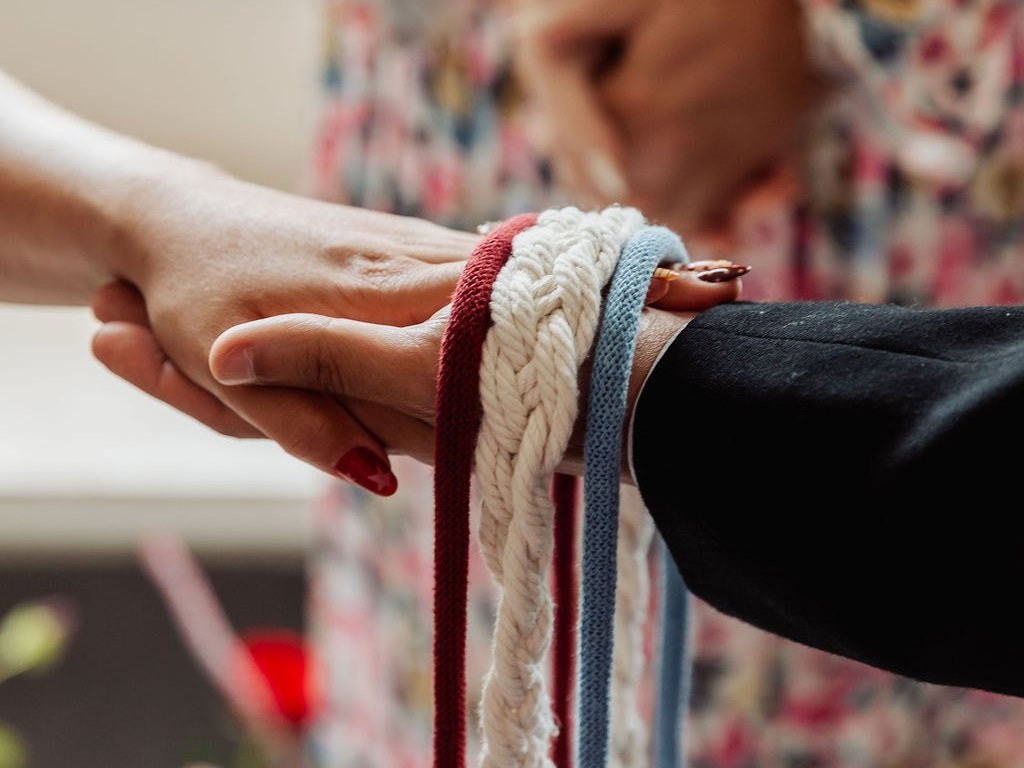 Handfasting cords tied around a couple's joined hands, Jan standing behind them
