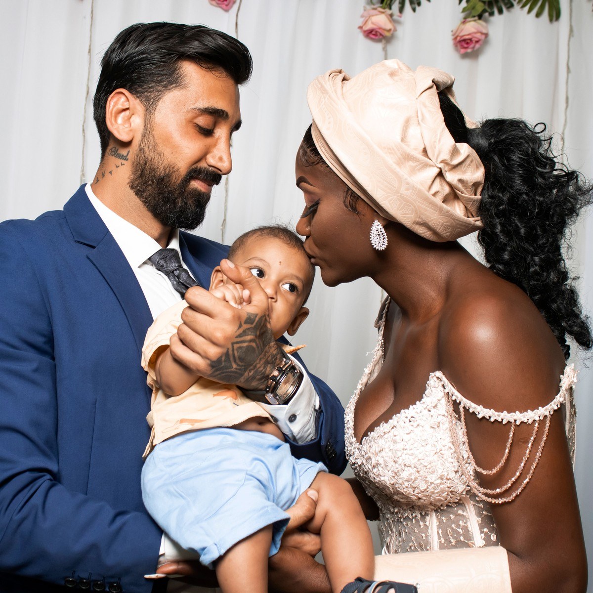 A father holds his baby son while the baby's mother kisses his forehead