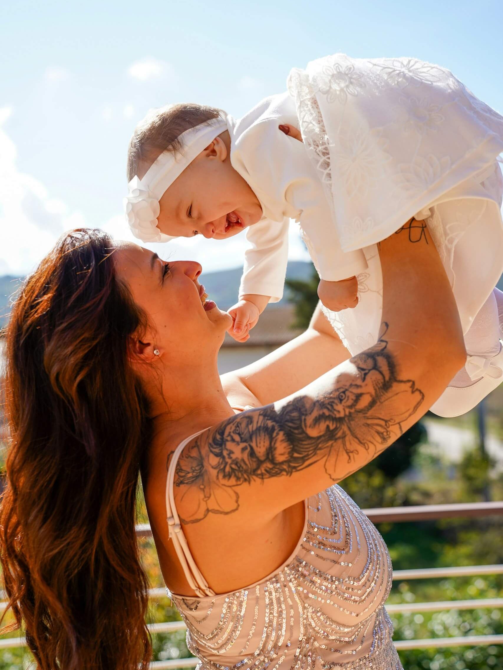 A laughing mother lifts her baby high into a bright sky