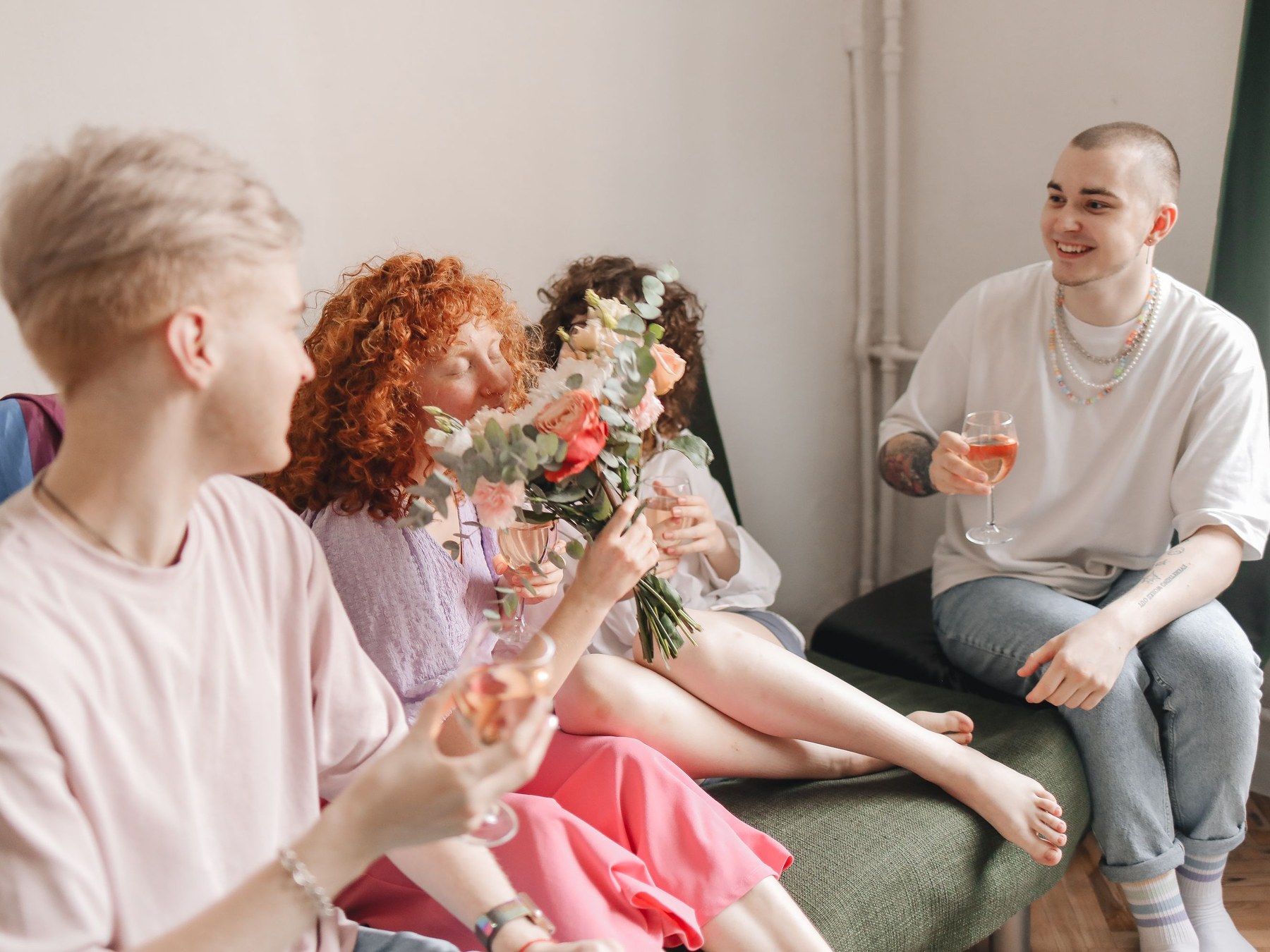 Four friends sitting together in a bright room with drinks and a bouquet of flowers, laughing