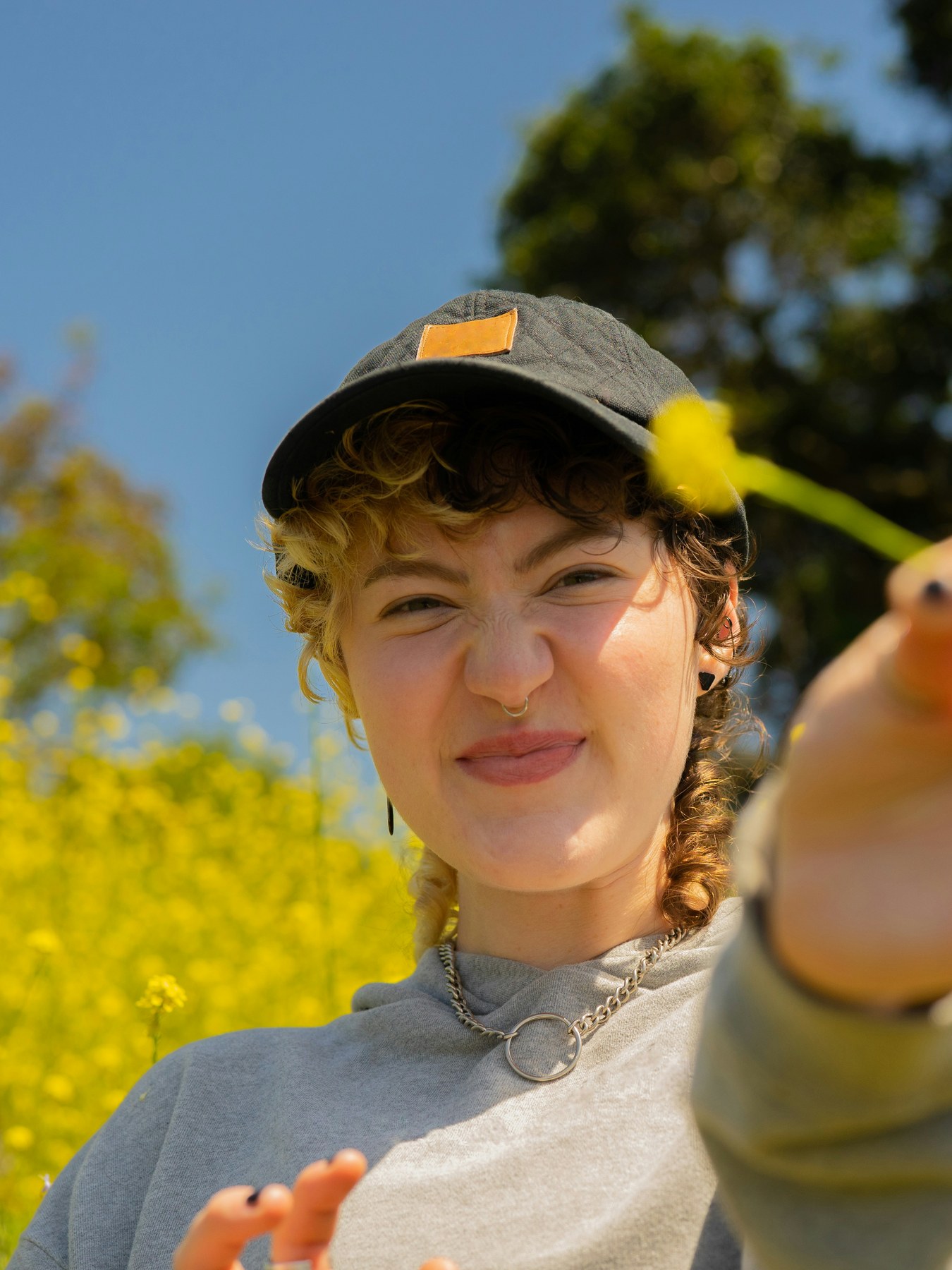 A young person in a cap holding out a wildflower, standing in a field of yellow rapeseed